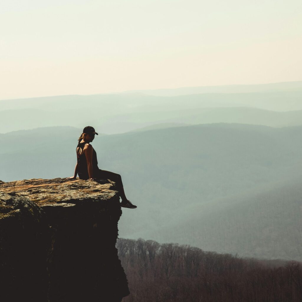 Woman sitting on a cliff edge overlooking a vast mountain landscape in Arkansas.