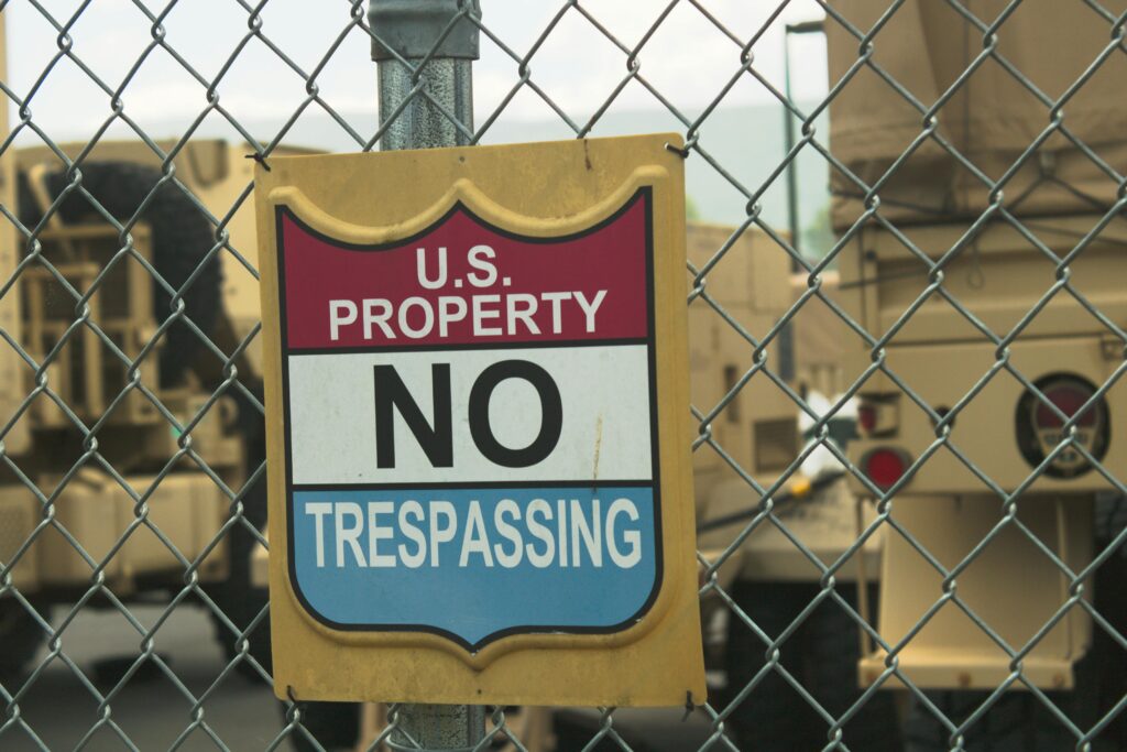 A no trespassing sign on a chain link fence at a U.S. property in Nevada with military vehicles in the background.