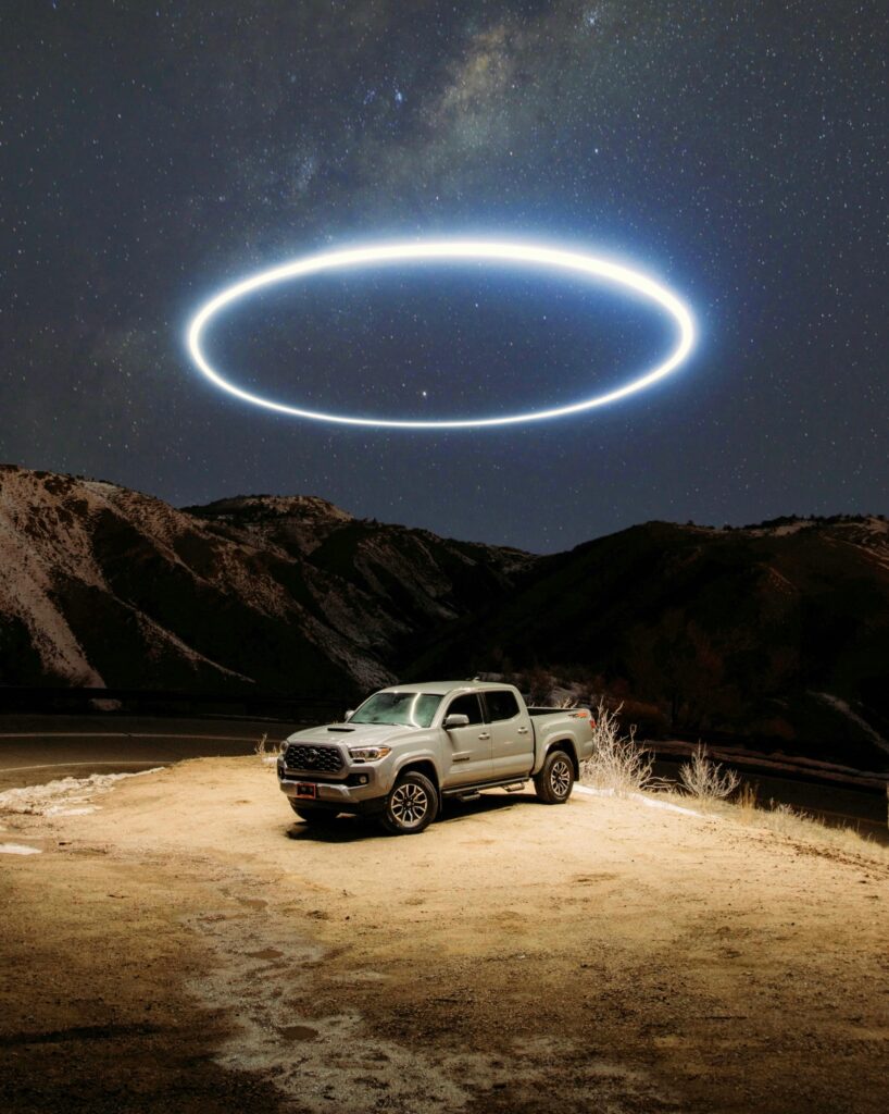 A pickup truck parked under a starry night sky, highlighted by a mysterious circular light formation.