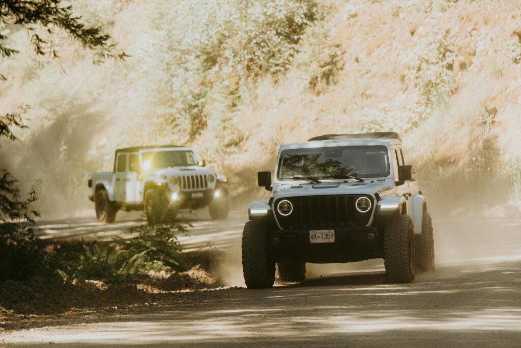 Two jeeps speeding through a dusty, forested road, creating an adventurous off-road scene.