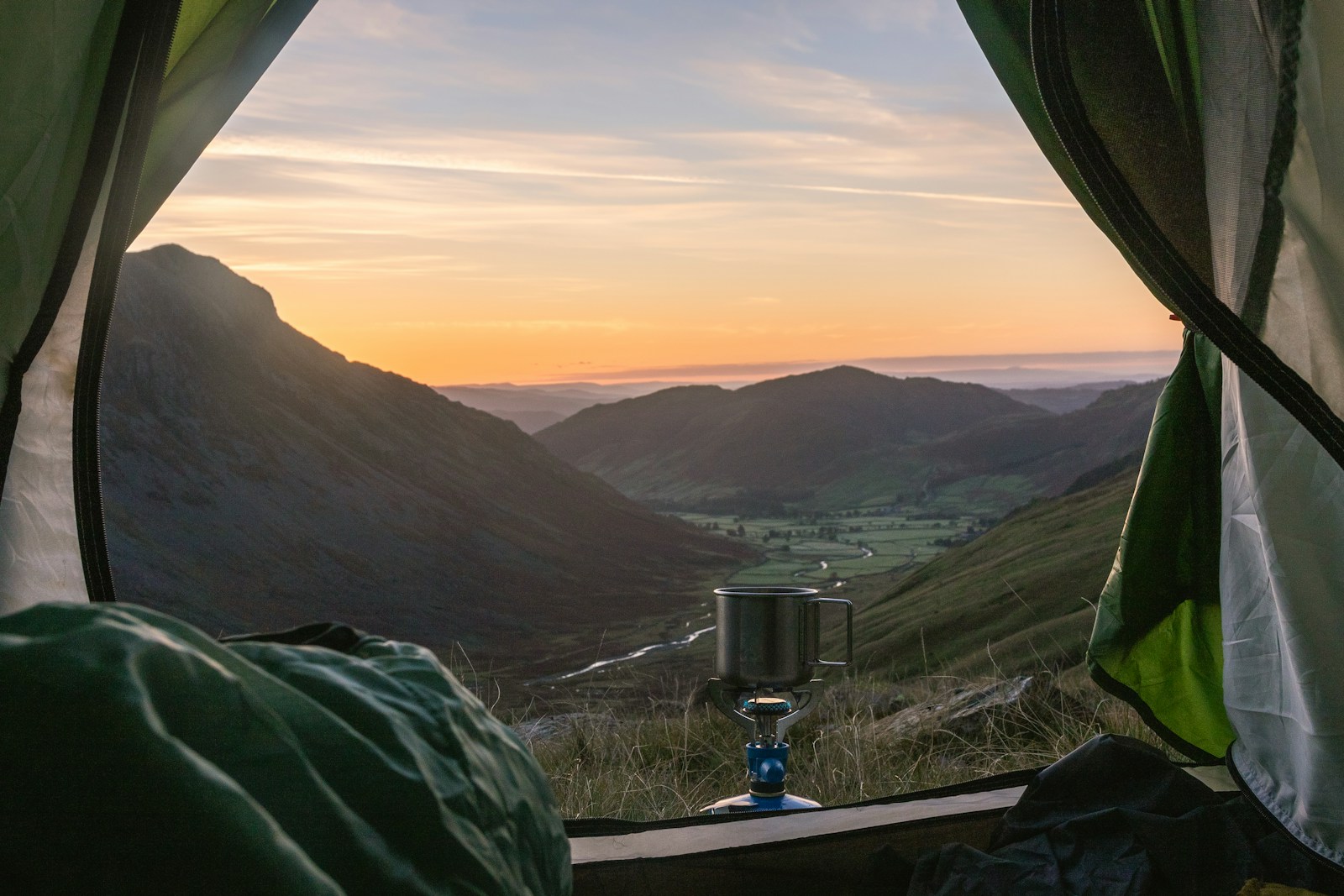 green and brown mountains during sunrise looking out a tent door
