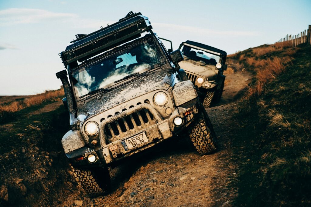 Two jeeps are driving off-road, covered in mud.