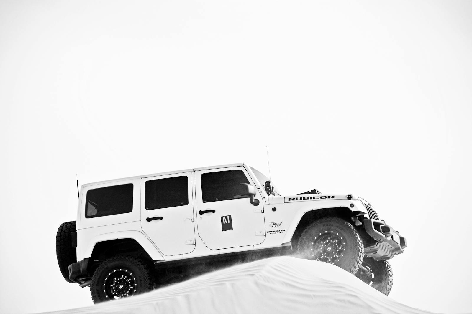 Dynamic shot of a Jeep climbing a sand dune in a black and white landscape, showcasing adventure.